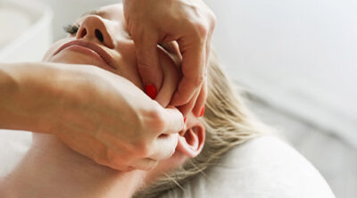 Derma Anti-Aging Massage mit pflegenden Griffen an Wangen und Kieferpartie einer Kundin auf der Massageliege