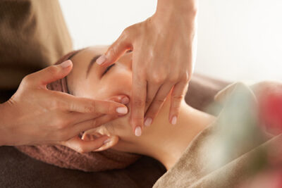 Kosmetische Lymphdrainage mit sanften Griffen an Stirn und Schläfen einer entspannt liegenden Kundin